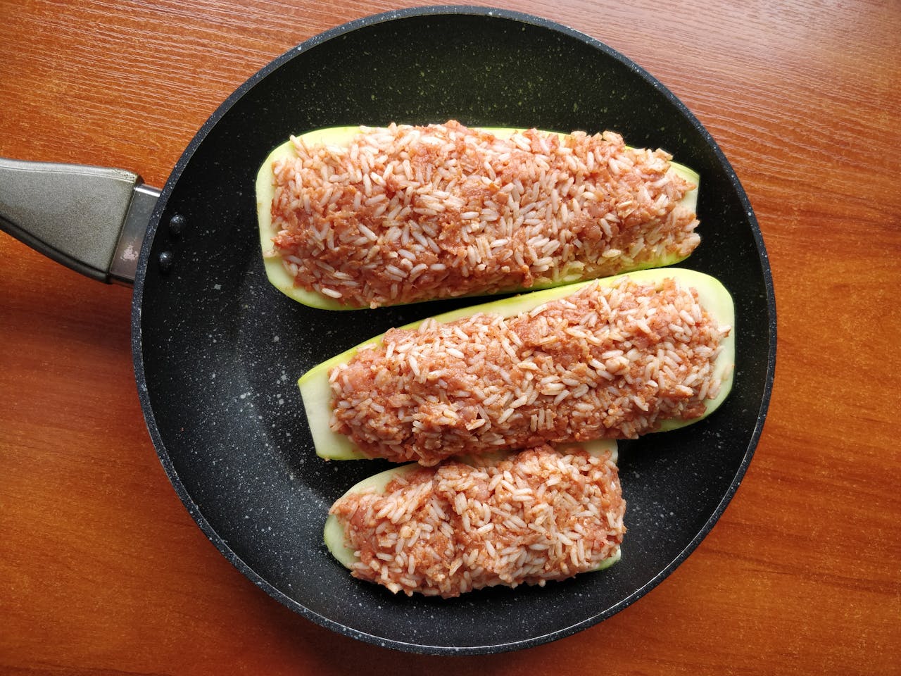 heros-img Appetizing stuffed zucchini with rice, served in a skillet on a wooden table.