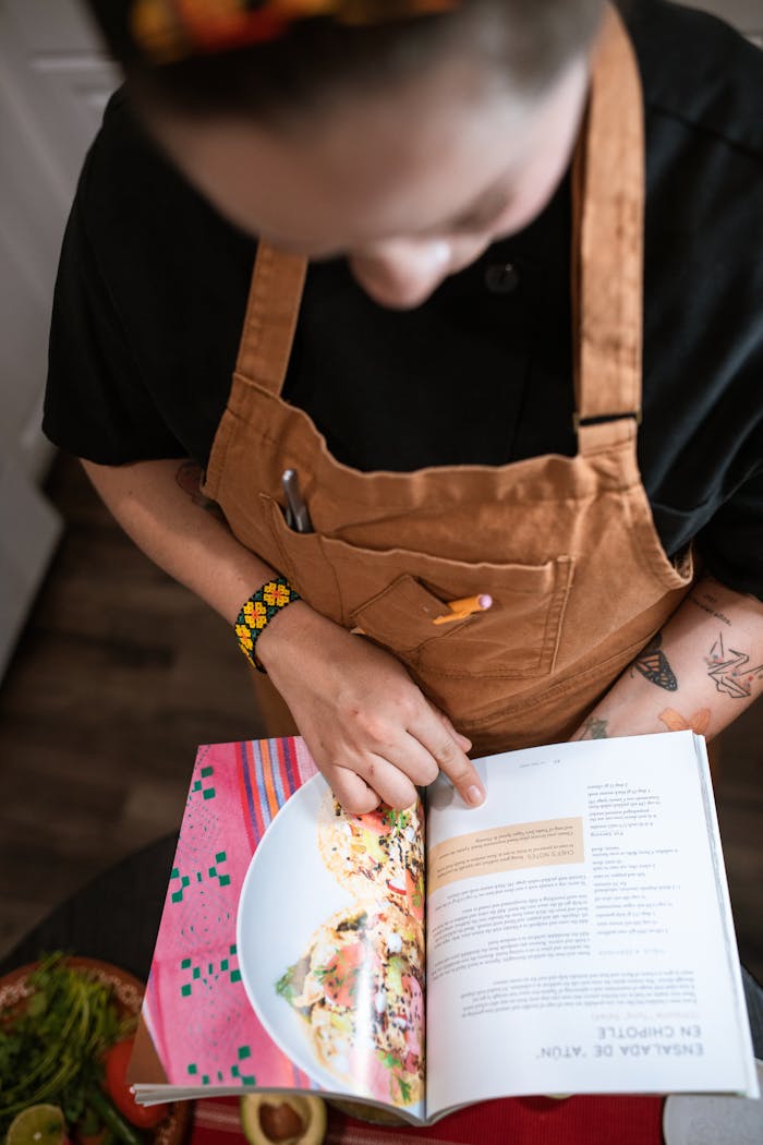 our-story A chef in a brown apron reading a cookbook for recipe guidance while cooking indoors.